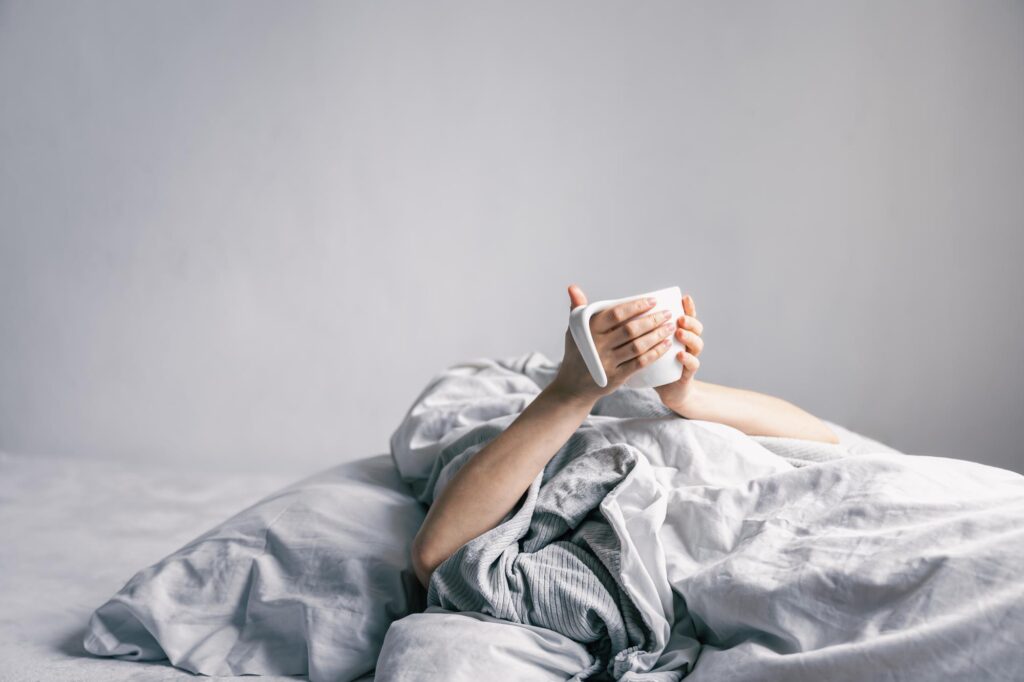 womans-hand-holds-cup-coffee-while-lying-bed.